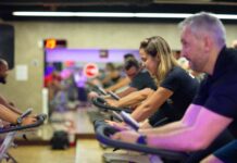 Alunos homens e mulheres pedalando em aula de bike na academia.