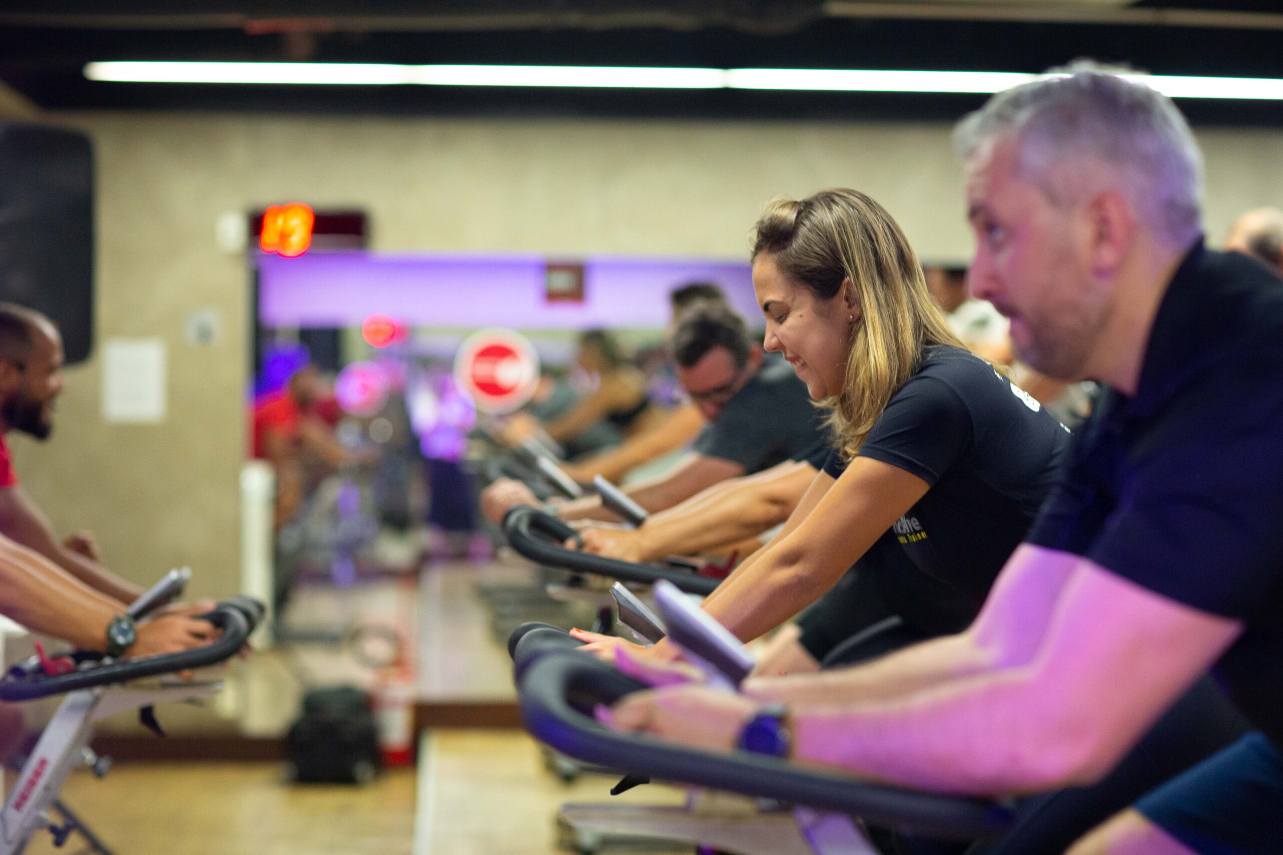 Alunos homens e mulheres pedalando em aula de bike na academia.