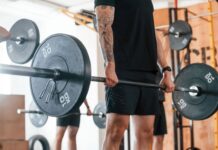 Homem segurando barra com anilhas para fazer exercício stiff.