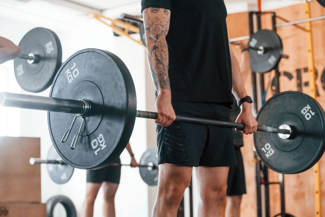 Homem segurando barra com anilhas para fazer exercício stiff.