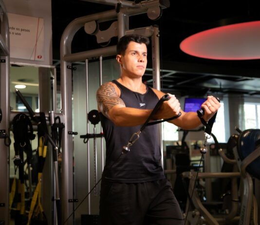 Homem puxando polia para membros superiores em treino full body masculino.