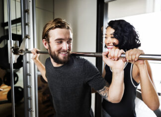 Exercícios de musculação: guia completo para iniciantes e intermediários Homem realizando agachamento com barra em academia enquanto mulher o auxilia como instrutora.