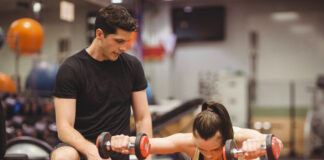 Mulher fazendo exercício com halteres sobre bola de estabilidade com acompanhamento de personal trainer na academia