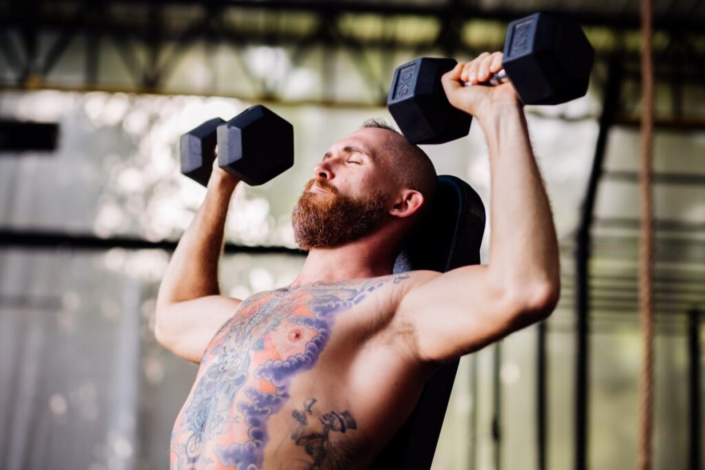Homem tatuado fazendo desenvolvimento Arnold na academia Homem tatuado fazendo desenvolvimento Arnold na academia.