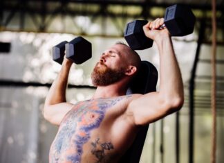 Homem tatuado fazendo desenvolvimento Arnold na academia.
