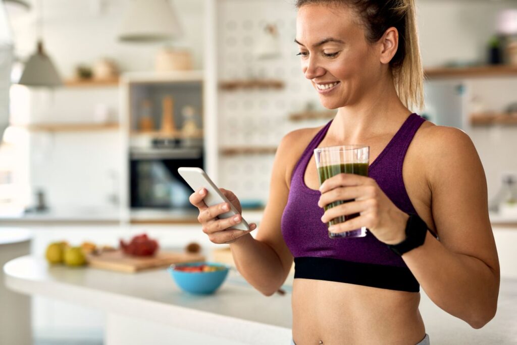 Mulher sorridente toma suco verde em cozinha saudável, representando o uso consciente da glutamina na rotina fitness Mulher sorridente toma suco verde em cozinha saudável, representando o uso consciente da glutamina na rotina fitness.