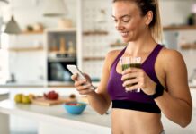 Mulher sorridente toma suco verde em cozinha saudável, representando o uso consciente da glutamina na rotina fitness.