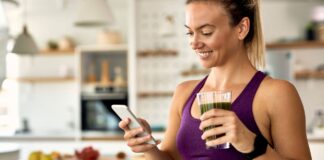 Mulher sorridente toma suco verde em cozinha saudável, representando o uso consciente da glutamina na rotina fitness.