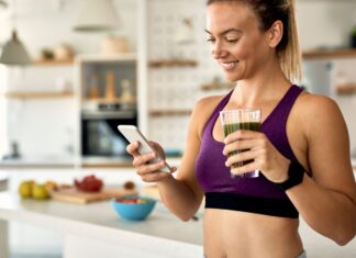 Mulher sorridente toma suco verde em cozinha saudável, representando o uso consciente da glutamina na rotina fitness.