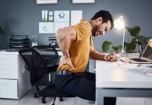 Homem sentado com dor nas costas mostra os efeitos do sedentarismo e da má postura, destacando a importância de se exercitar.