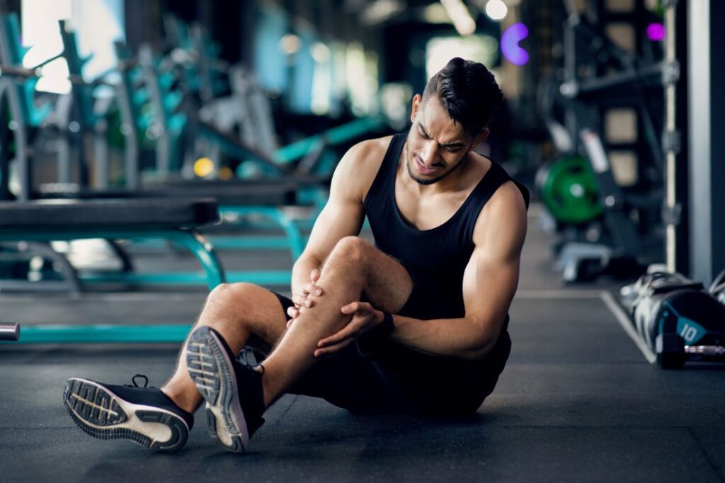Jovem com dor na perna após treino na academia Jovem com dor na perna após treino, ilustrando o impacto do esforço físico e má circulação nas dores nas pernas.