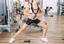 Mulher realizando exercício de resistência com faixa elástica na academia para fortalecer as pernas e melhorar a circulação.