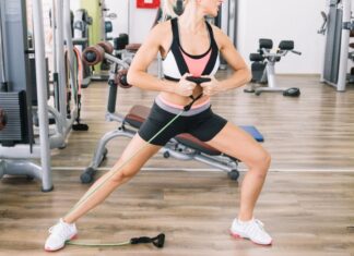 Mulher realizando exercício de resistência com faixa elástica na academia para fortalecer as pernas e melhorar a circulação.