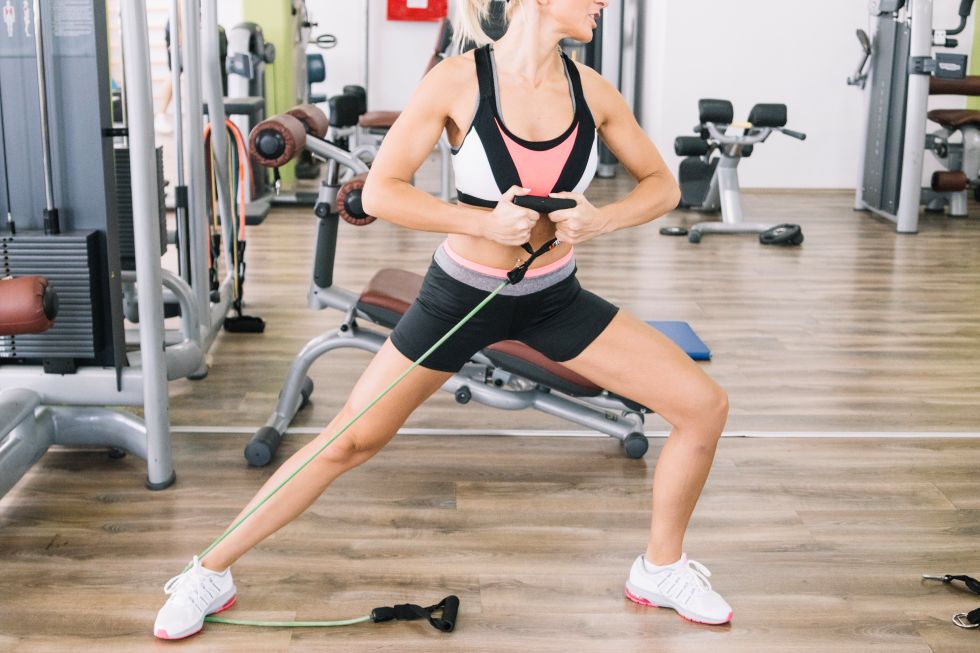 Mulher realizando exercício de resistência com faixa elástica na academia para fortalecer as pernas e melhorar a circulação.
