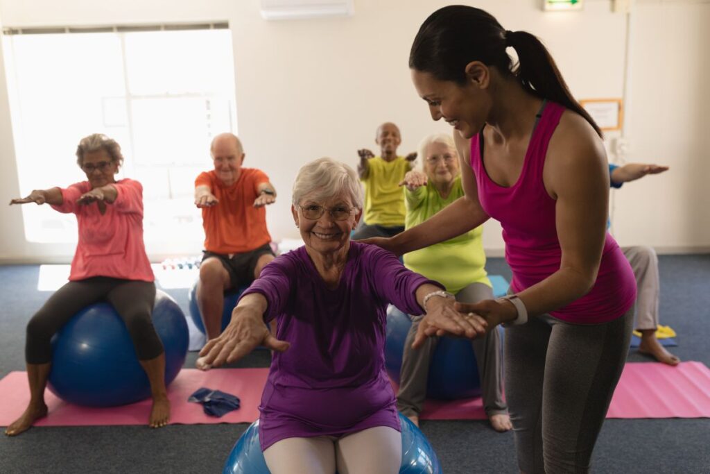 Idosos praticando pilates com bola em grupo, promovendo equilíbrio, mobilidade e bem-estar na terceira idade com acompanhamento profissional.
