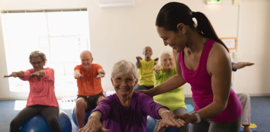 Idosos praticando pilates com bola em grupo, promovendo equilíbrio, mobilidade e bem-estar na terceira idade com acompanhamento profissional.