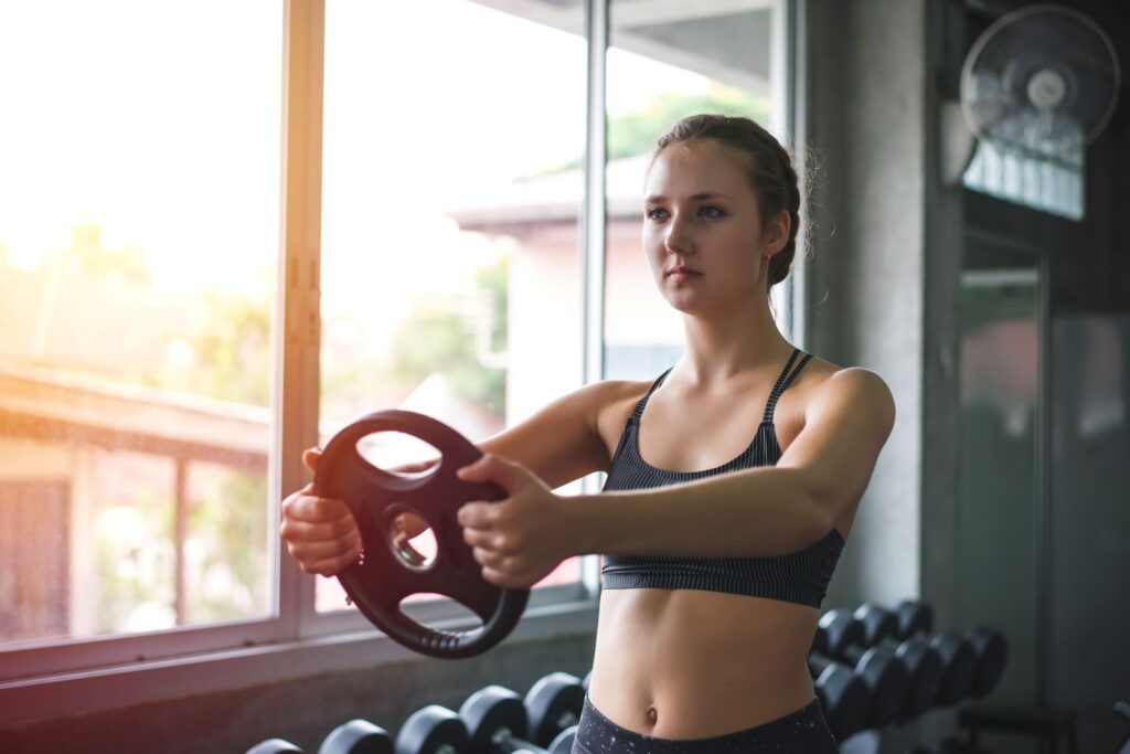 Mulher jovem realizando exercício de fortalecimento com anilha na academia Mulher jovem realizando exercício de fortalecimento com anilha na academia para auxiliar no controle do diabetes.
