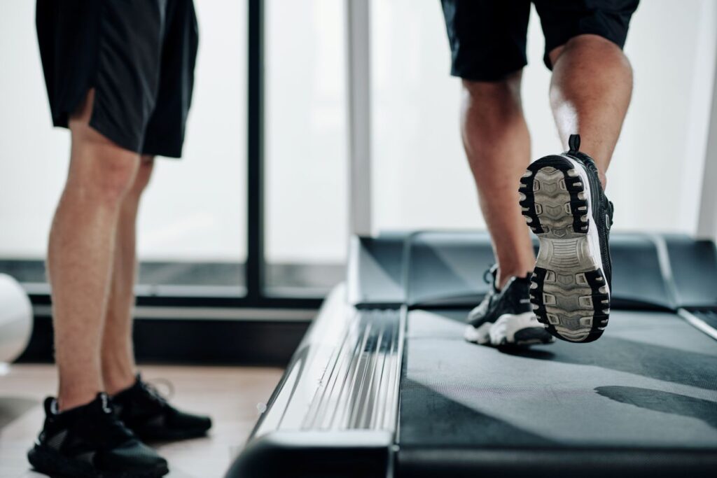 Pessoa caminhando em esteira sob orientação de treinador, prática de exercício físico. Pessoa caminhando em esteira sob orientação de treinador, prática de exercício físico para controle do diabetes.