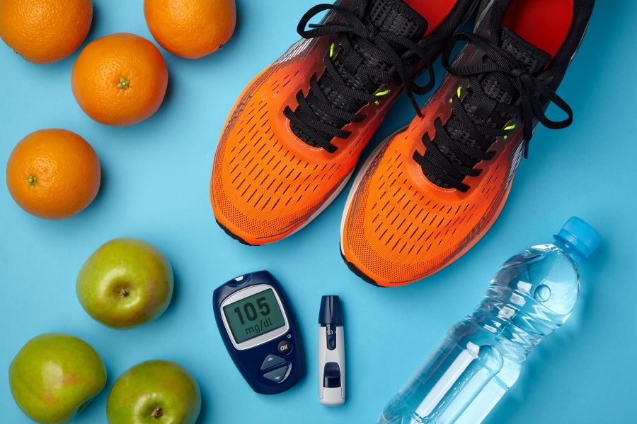Itens como tênis, frutas, glicômetro e água sobre fundo azul. Itens como tênis, frutas, glicômetro e água sobre fundo azul simbolizam o controle do diabetes com hábitos saudáveis e exercício físico.