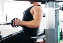 Homem realiza uma remada baixa com triângulo, um exercício de musculação, ele está no pico do movimento, exibindo a correta retração escapular para máxima contração muscular.