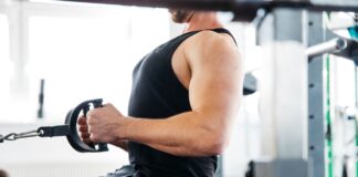 Homem realiza uma remada baixa com triângulo, um exercício de musculação, ele está no pico do movimento, exibindo a correta retração escapular para máxima contração muscular.