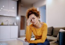 Mulher jovem com expressão de preocupação sentada no sofá, representando estresse e necessidade de aprender como diminuir a ansiedade com exercícios e respiração.