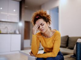 Mulher jovem com expressão de preocupação sentada no sofá, representando estresse e necessidade de aprender como diminuir a ansiedade com exercícios e respiração.