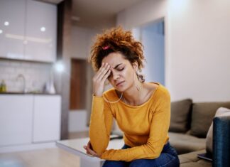 Como aliviar o estresse: 7 estratégias eficazes com exercícios Mulher jovem com expressão de preocupação sentada no sofá, representando estresse e necessidade de aprender como diminuir a ansiedade com exercícios e respiração.