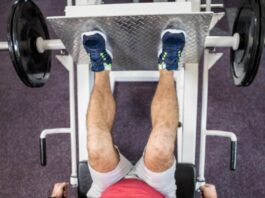 Erros no leg press 90 que podem travar seus resultados (e como corrigir) Pessoa realizando exercício no leg press 90 em academia, com pés na plataforma e pesos laterais, trabalhando músculos das pernas.