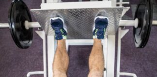 Pessoa realizando exercício no leg press 90 em academia, com pés na plataforma e pesos laterais, trabalhando músculos das pernas.