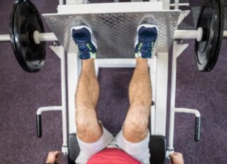 Erros no leg press 90 que podem travar seus resultados (e como corrigir) Pessoa realizando exercício no leg press 90 em academia, com pés na plataforma e pesos laterais, trabalhando músculos das pernas.