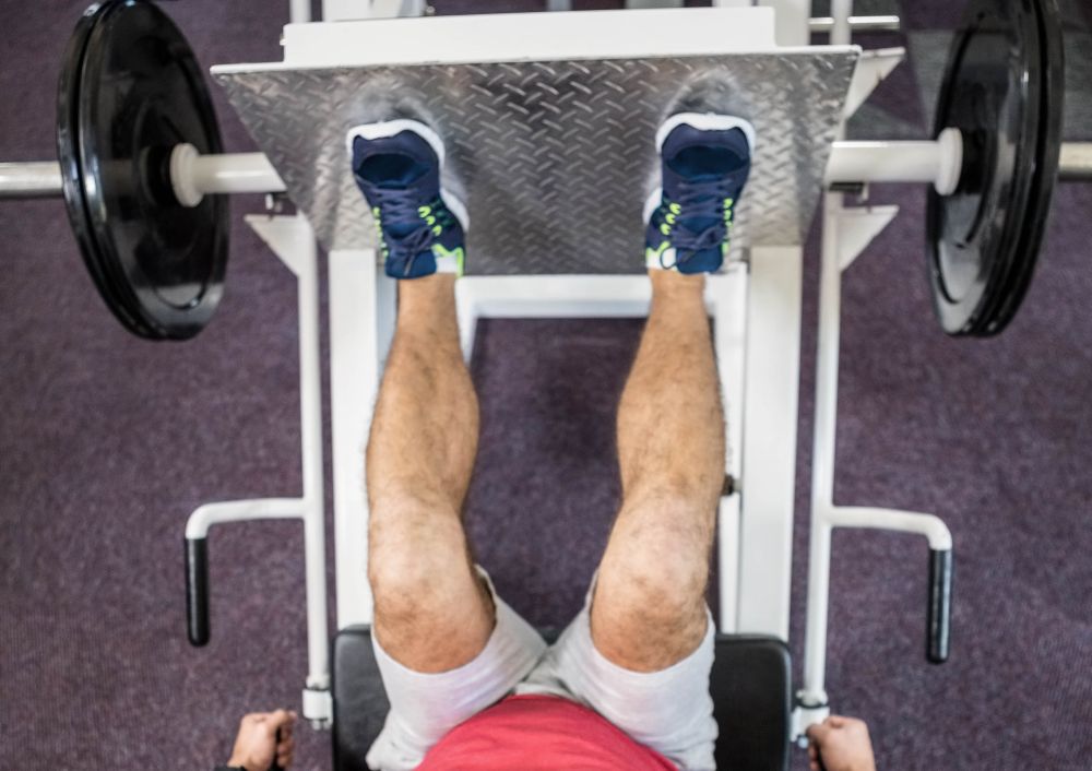 Pessoa realizando exercício no leg press 90 em academia, com pés na plataforma e pesos laterais, trabalhando músculos das pernas.