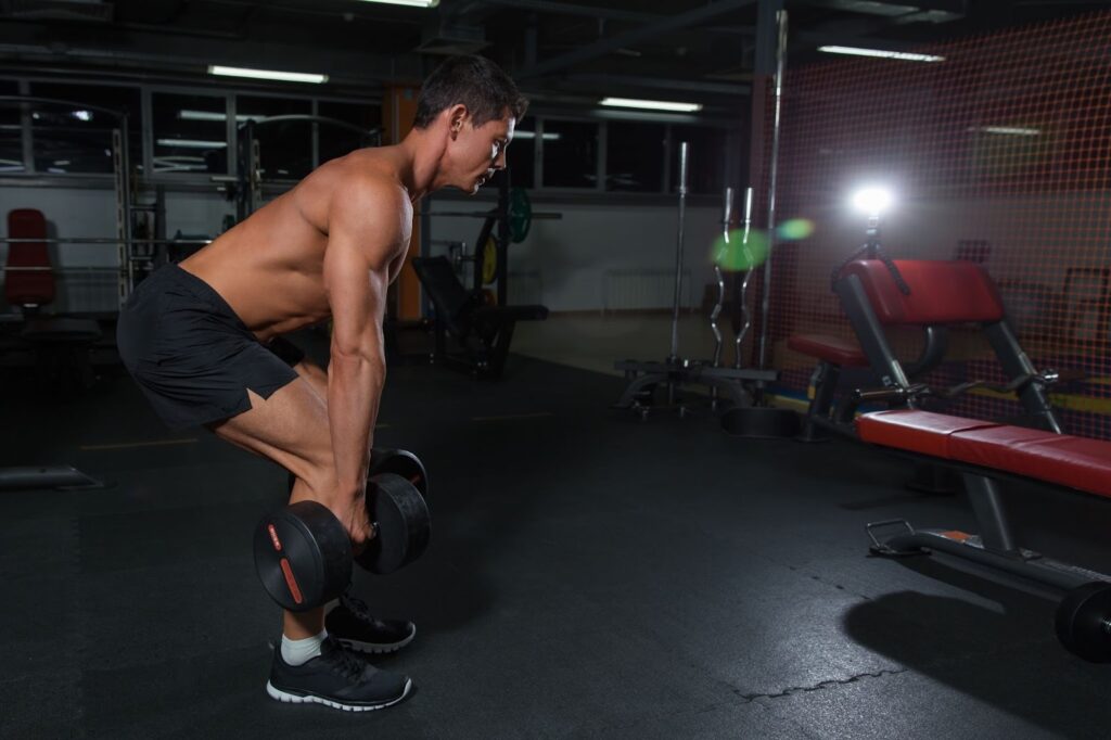 Segure um halter próximo ao peito, mantenha o tronco ereto e os pés afastados na largura dos ombros. Agache levando o quadril para trás até as coxas ficarem paralelas ao chão. Retorne à posição inicial empurrando o solo.