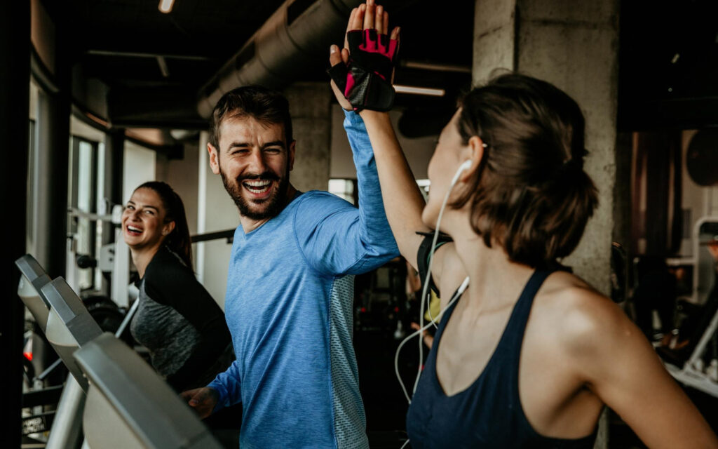 Um homem e mulher na esteira, celebrando com um "high five" após o treino na Cia Athletica, demonstrando como os exercícios em grupo promovem bem-estar e ajudam no controle da ansiedade.