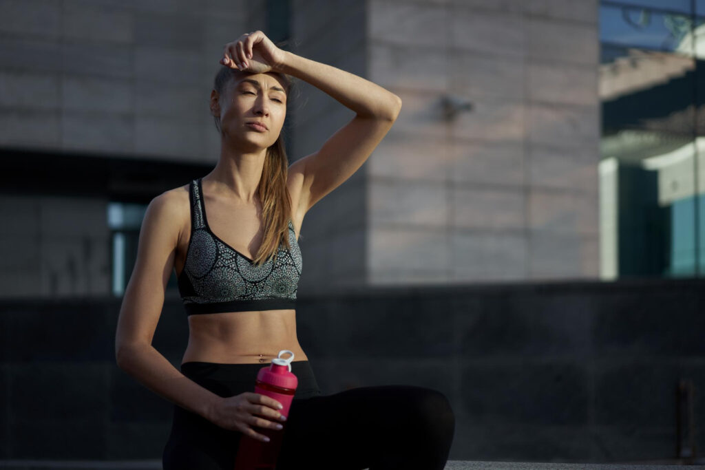 Mulher com expressão de cansaço após exercício segurando squeeze - sinais físicos do estresse no corpo feminino