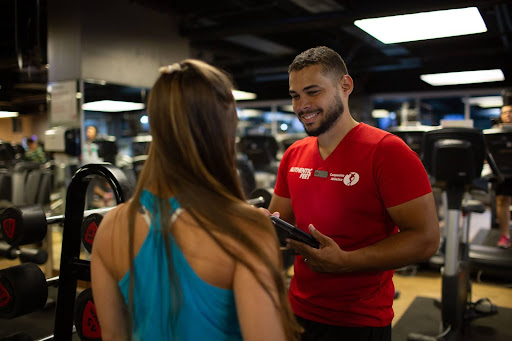 Professor da Cia Athletica orientando aluna na academia com tablet em mãos durante acompanhamento personalizado