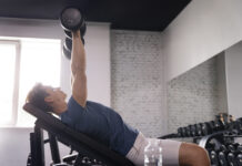 homem realizando exercício com halter em banco inclinado na academia, trabalhando a região do peitoral superior com foco na técnica correta.