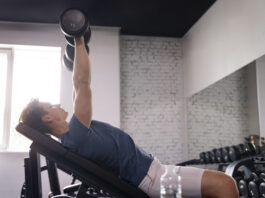 homem realizando exercício com halter em banco inclinado na academia, trabalhando a região do peitoral superior com foco na técnica correta.