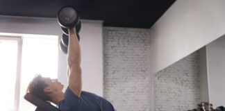 homem realizando exercício com halter em banco inclinado na academia, trabalhando a região do peitoral superior com foco na técnica correta.