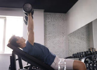 homem realizando exercício com halter em banco inclinado na academia, trabalhando a região do peitoral superior com foco na técnica correta.