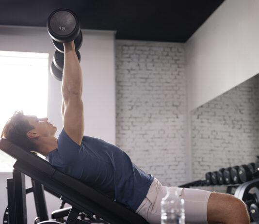 homem realizando exercício com halter em banco inclinado na academia, trabalhando a região do peitoral superior com foco na técnica correta.