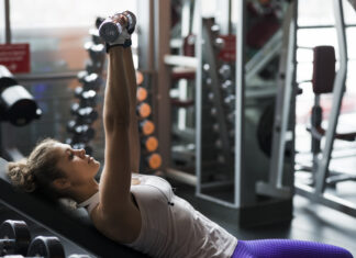 Exercícios para peito não são só sobre estética — são sobre postura e força real Mulher realizando exercício de peito com halteres em banco inclinado na academia.