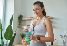 Mulher com roupa de academia preparando suplemento em coqueteleira na cozinha