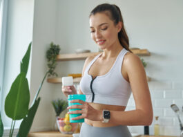 Mulher com roupa de academia preparando suplemento em coqueteleira na cozinha