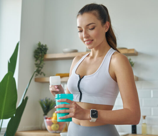 Mulher com roupa de academia preparando suplemento em coqueteleira na cozinha