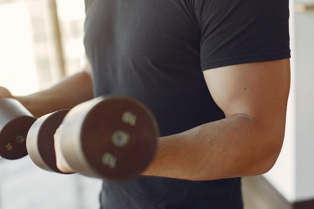 Homem treinando braços com halteres em academia.