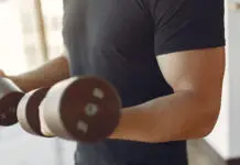 Homem treinando braços com halteres em academia.