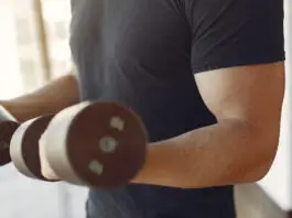 Exercícios para braços: quais músculos você trabalha e como organizá-los Homem treinando braços com halteres em academia.