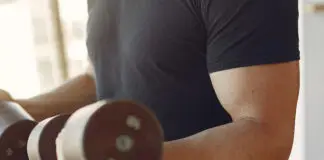Homem treinando braços com halteres em academia.