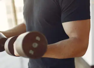 Homem treinando braços com halteres em academia.
